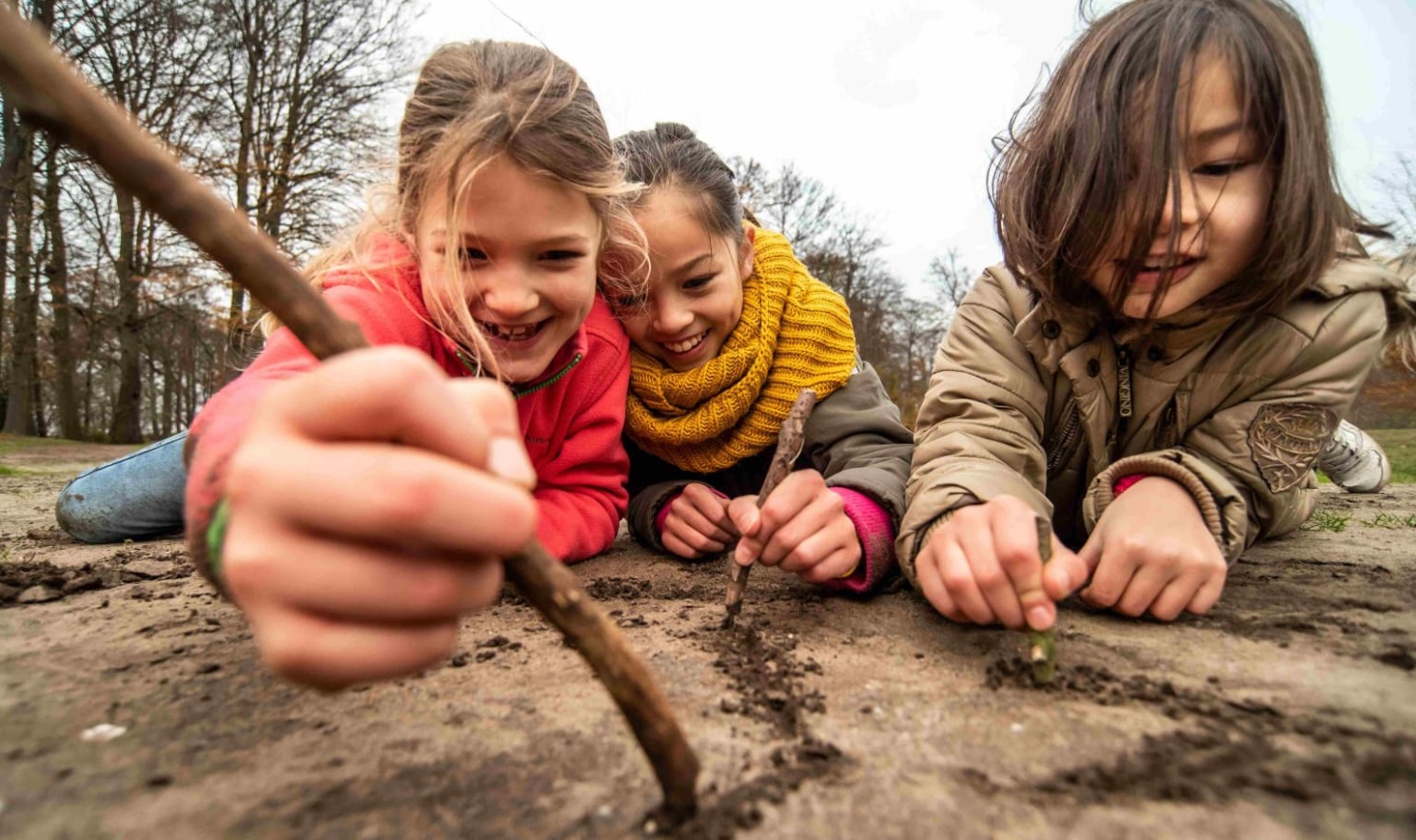 Drie kinderen tekenen in de aarde met stokjes