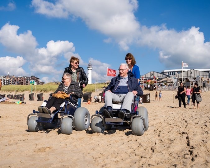 Twee personen worden in strandrolstoelen worden over het strand bij Egmond gereden.