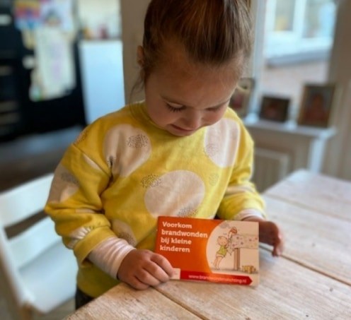 Een meisje presenteert het boekje "Voorkom brandwonden bij kleine kinderen"